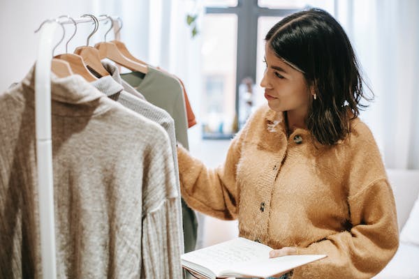 Smiling designer with notebook against assorted clothes